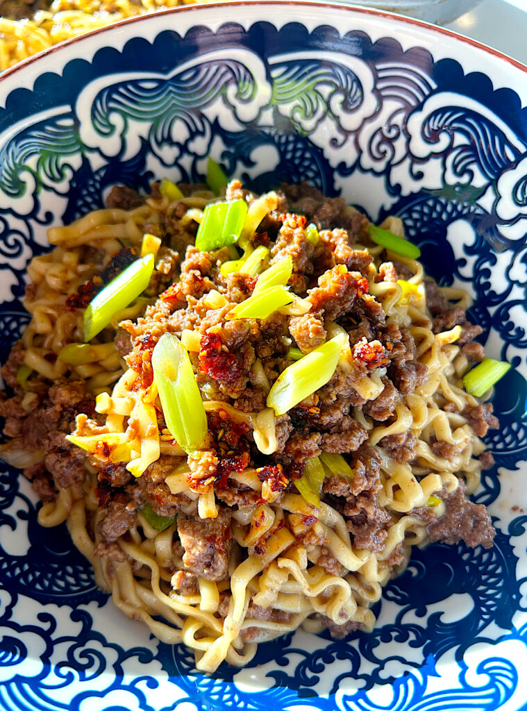 a blue and white bowl of noodles with ground venison, chili oil and green onions