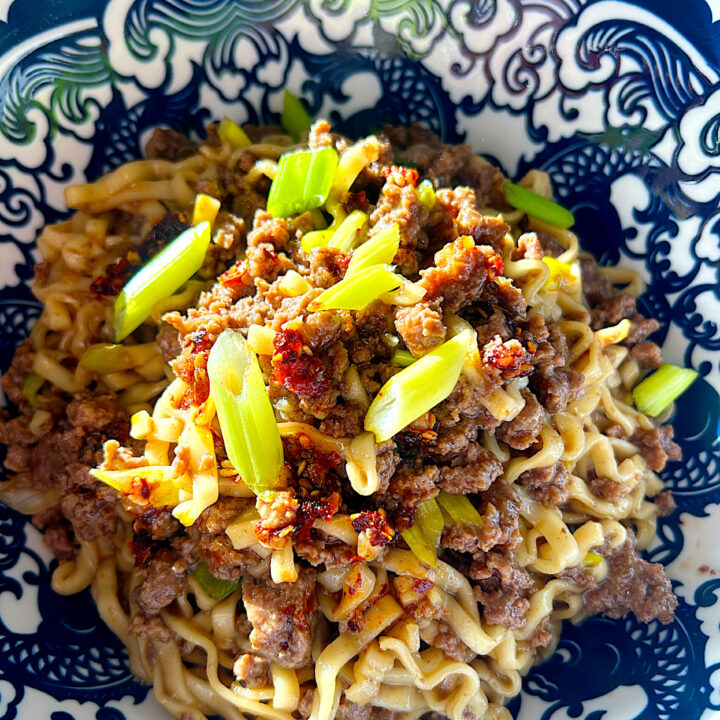 a blue and white bowl of noodles with ground venison, chili oil and green onions