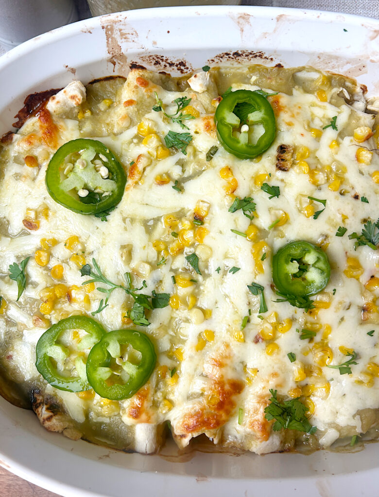 a baking dish full of enchiladas with green Chile sauce and jalapeños on top