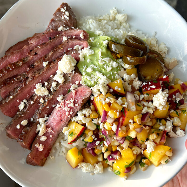 a white bowl with rice, sliced steak, peach and corn salsa and avocado sauce