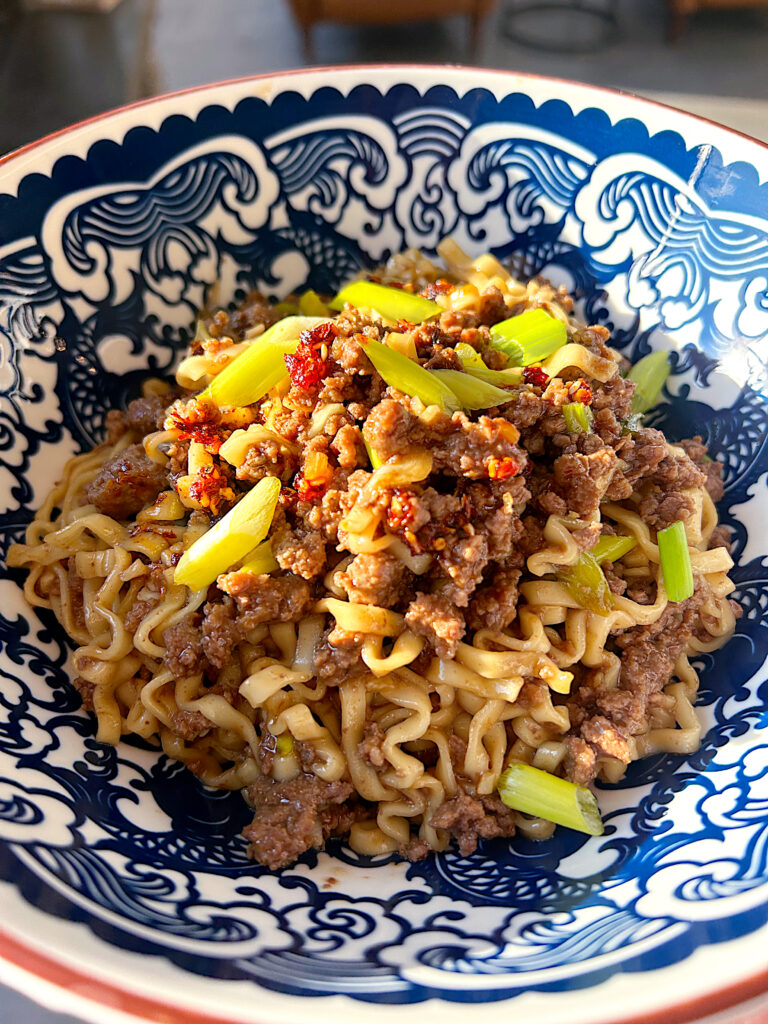 a bowl of ramen noodles with sweet and salty sauce, ground meat and green onions