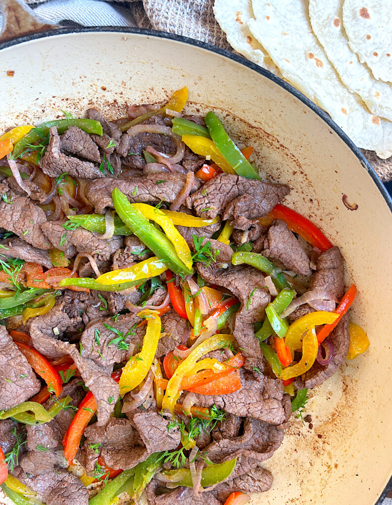 a skillet of cooked steak strips, and peppers and onions