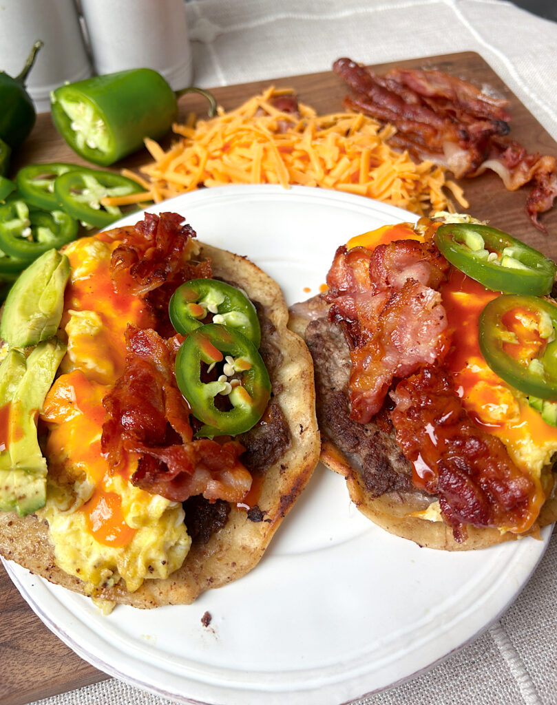 a white plate of breakfast tacos with sausage, eggs, cheese and avocado