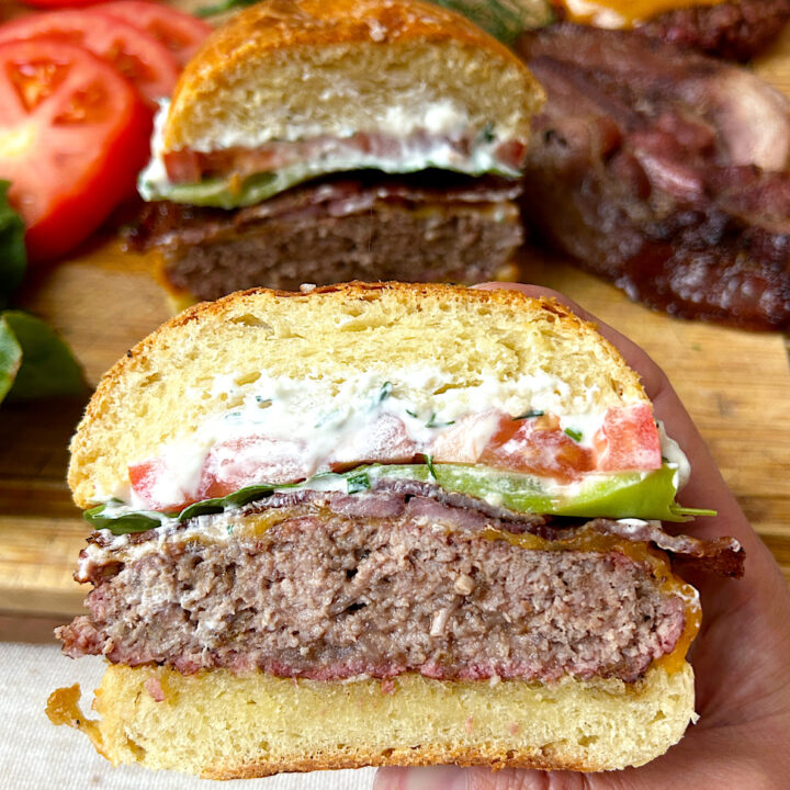 a brioche bun with a burger patty, lettuce, bacon and tomato cut in half