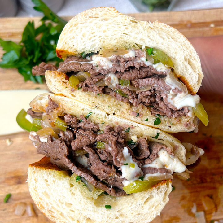 a Philly cheesesteak sandwich cut in half with steak, cheese and peppers