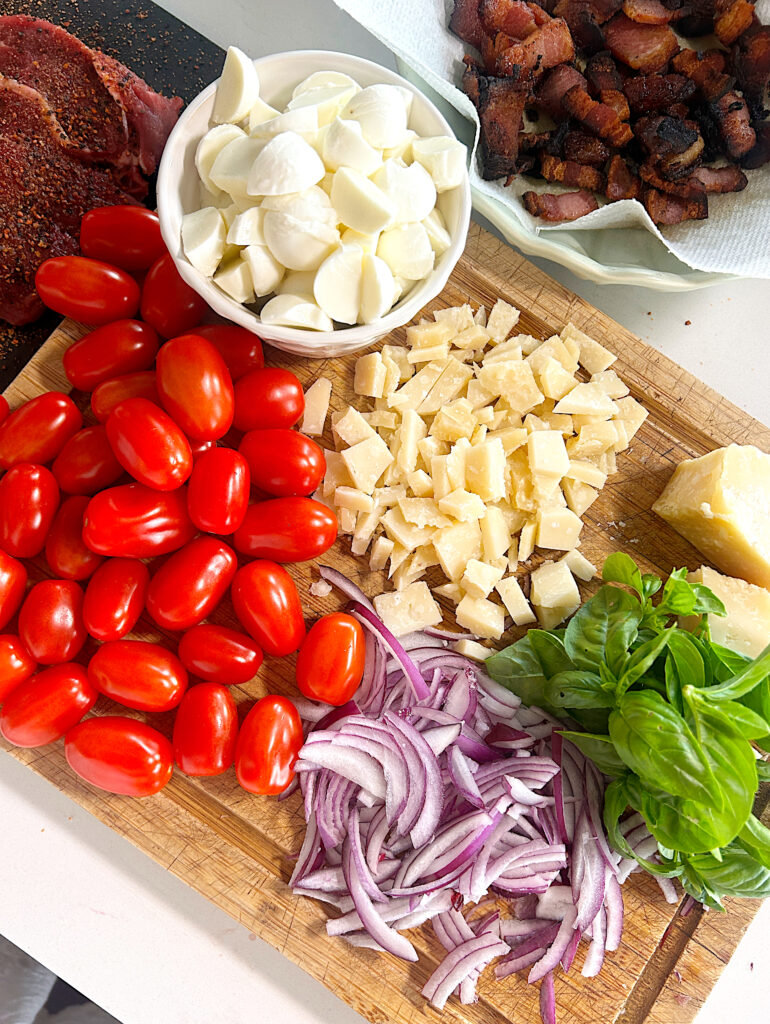 a wood board with tomatoes, cheese, basil and red onion