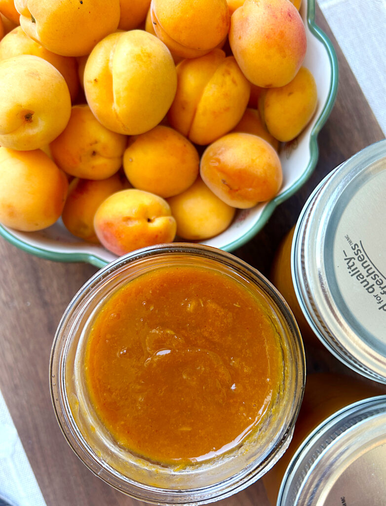 a jar of bbq sauce next to a bowl of fresh apricots