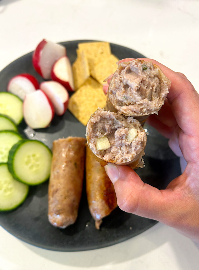 a plated of chopped vegetables and an apple turkey sausage cut in half