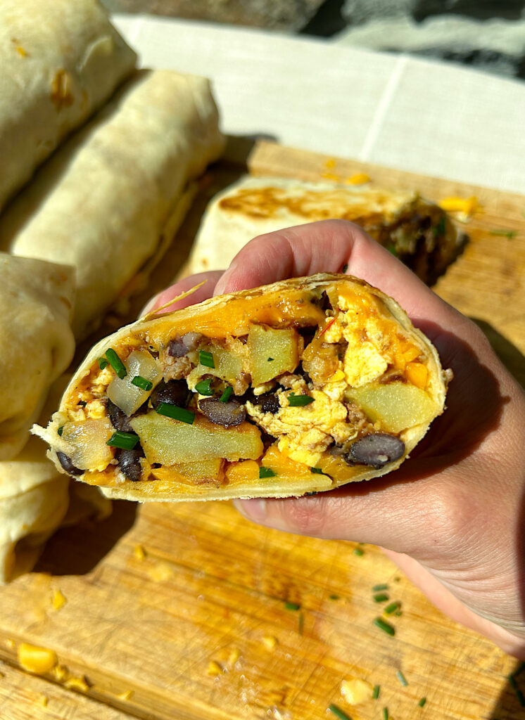 a breakfast burrito cut in half full of eggs, potato, venison, beans and cheese