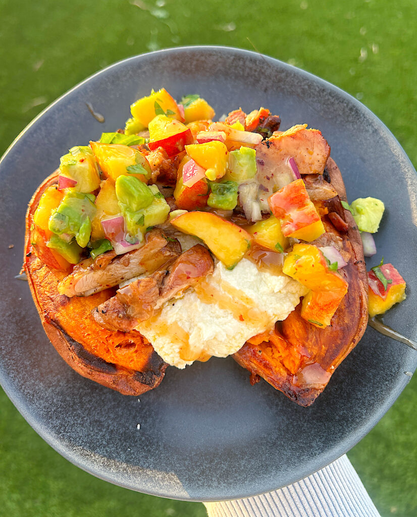 a black plate with a sweet potato topped with creamy feta cheese, chicken and peach salsa