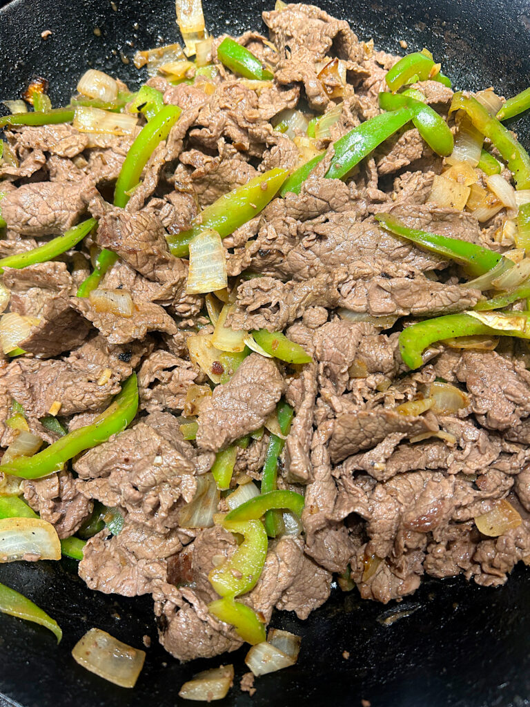 a skillet with thinly shaved venison and green peppers