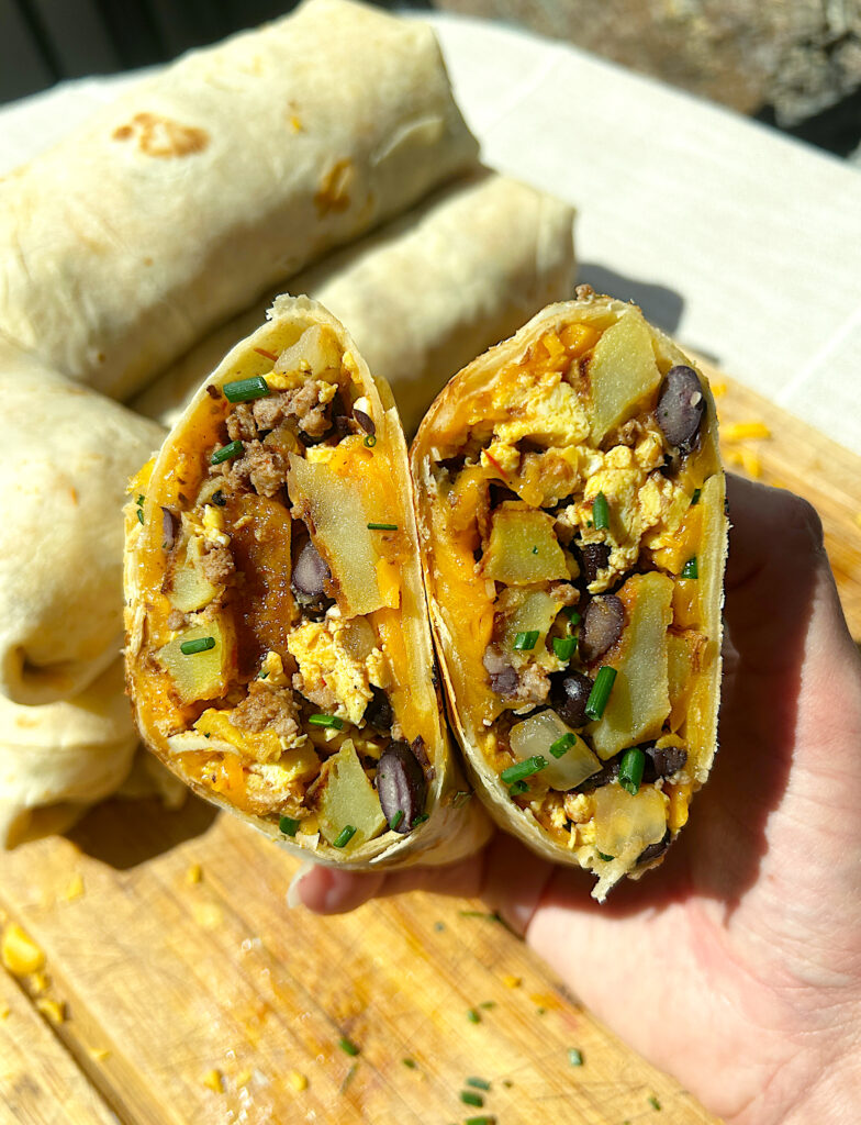 a breakfast burrito cut in half full of eggs, potatoes, meat and black beans