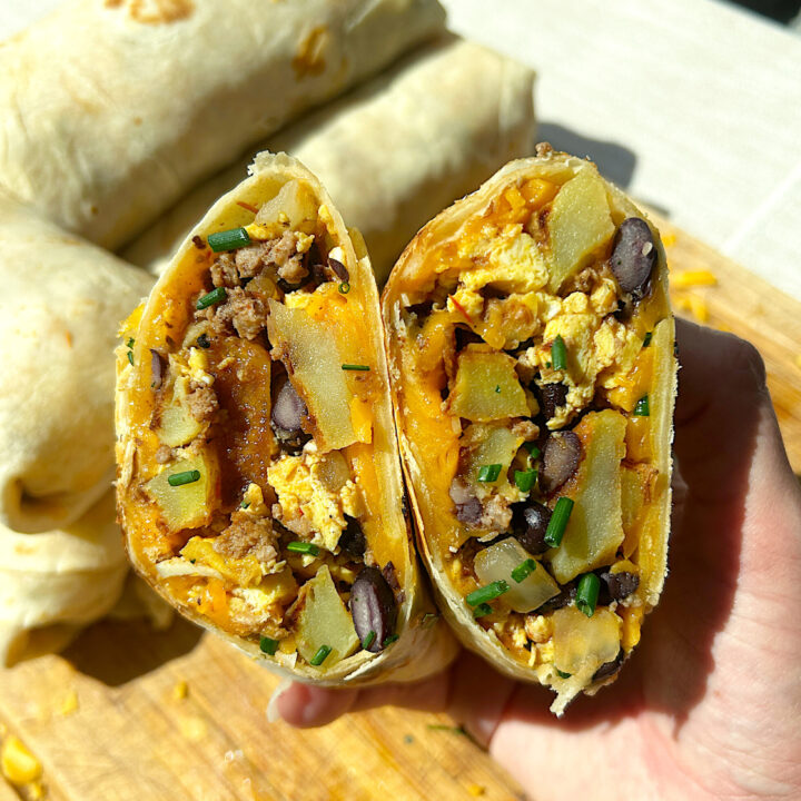 a breakfast burrito cut in half full of eggs, potatoes, meat and black beans