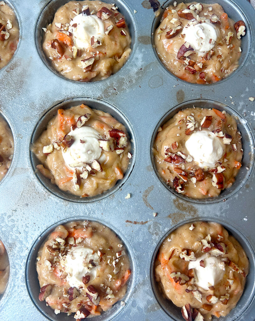 a muffin tin full of unbaked muffins stuffed with cream cheese