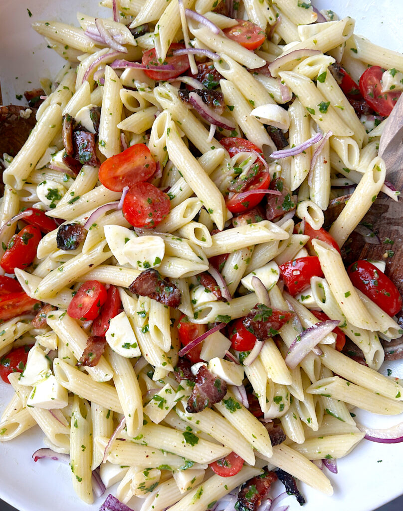 a bowl of pasta salad full of penne, tomatoes, mozzarella and bacon