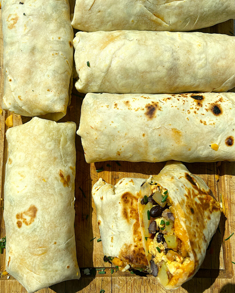 a bunch of breakfast burritos rolled up on a wood board