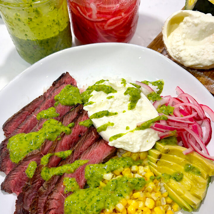 a whit bowl of rice with sliced steak, avocado, burrata cheese, corn and chimichurri sauce