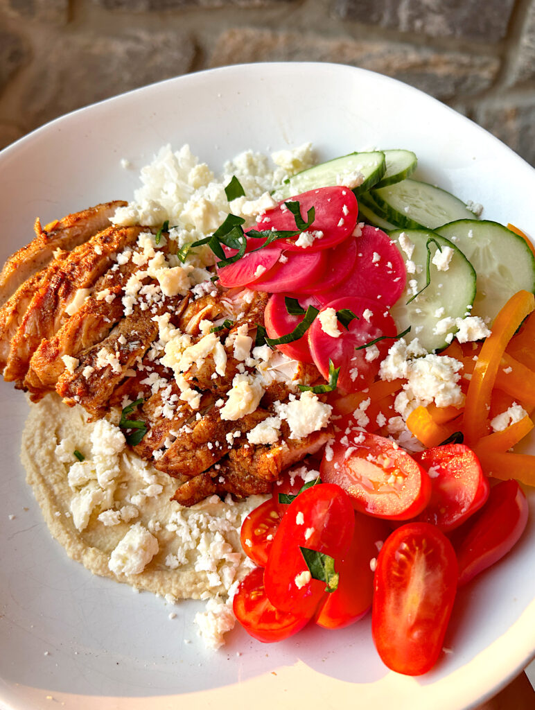 a rice bowl with hummus, tomatoes, pickled onions, chicken and feta cheese