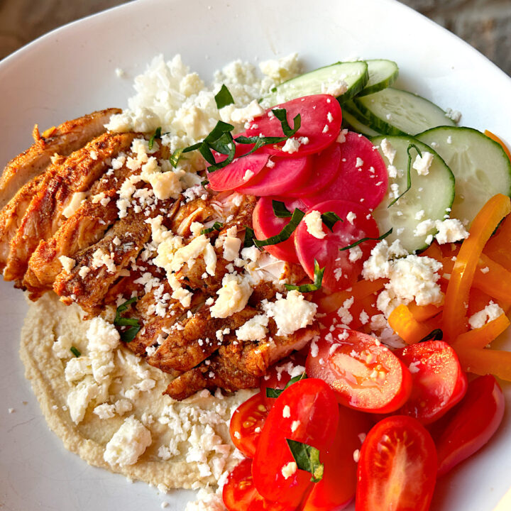 a rice bowl with hummus, tomatoes, pickled onions, chicken and feta cheese