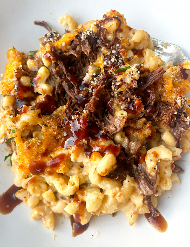a white bowl of macaroni and cheese with bbq sauce and shredded meat