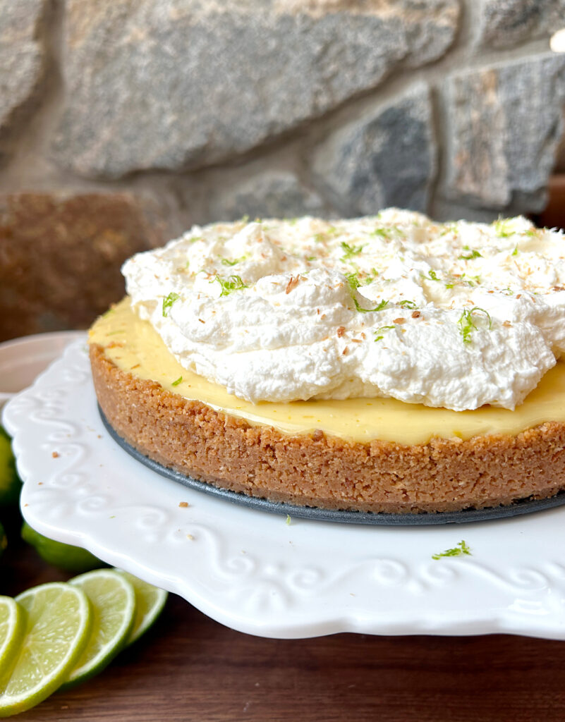 a key lime pie on a white plater, with graham crust and whipped cream on top