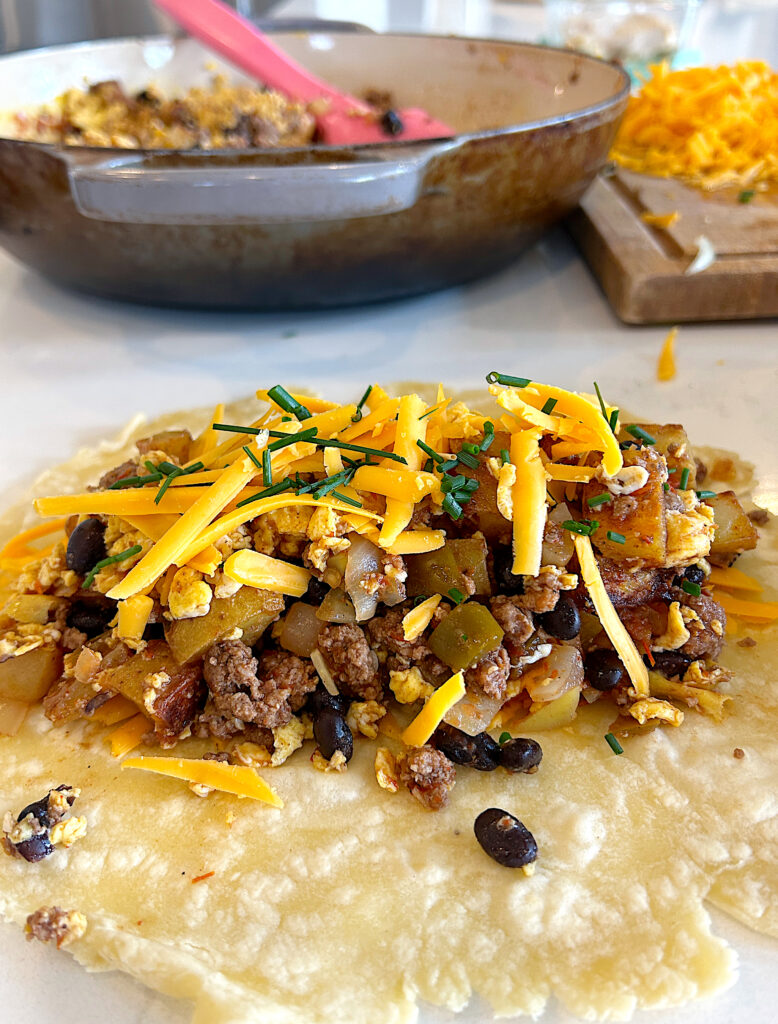 a tortilla topped with eggs, potatoes, meat, and cheese