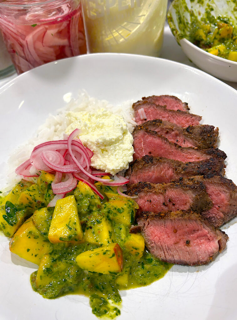a white bowl with rice, sliced steak, chiichurri, peaches and pickled onions