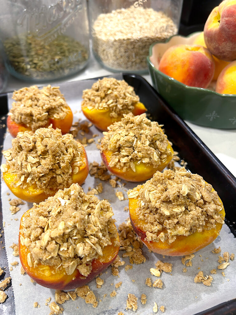 a baking sheet with peaches cut in half topped with an oatmeal crumble