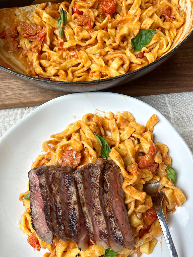 a bowl of cherry tomato and basil pasta with sliced steak on top