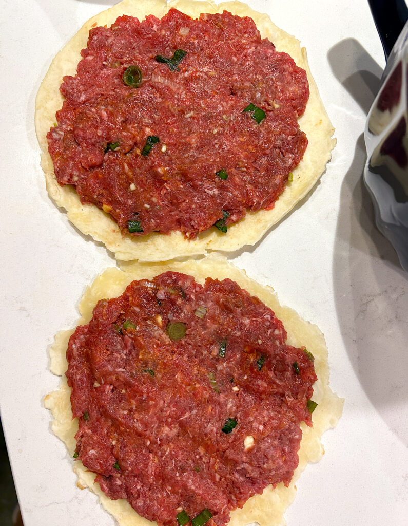 small tortilla with a layer of uncooked ground meat on top
