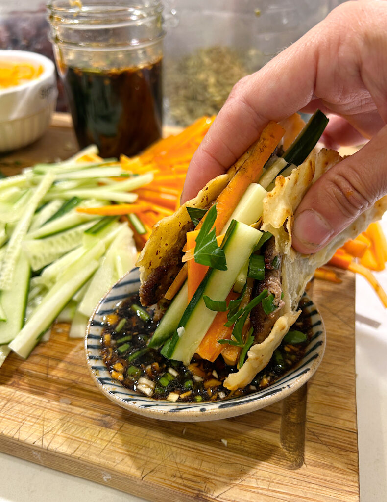 a dumpling flavoured taco being dipped into a soy and ginger dipping sauce