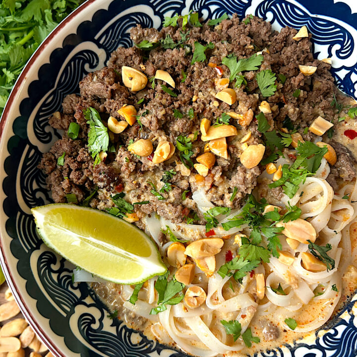 a blue and white bowl with rice noodle, ground meat, curry broth and fresh lime