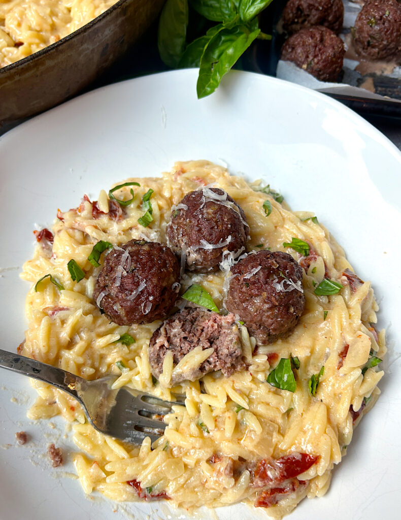 a white bowl of italian orzo pasta and venison meatballs on top