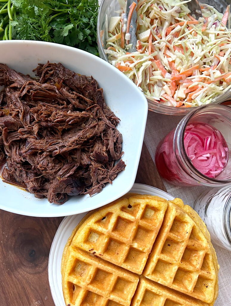 a plate of cornbread waffles, a bowl of shredded meat and a bowl of coleslaw