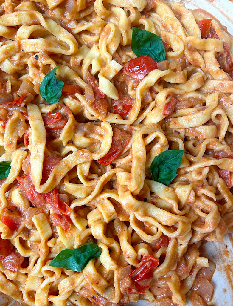 a skillet of linguini noodles with cherry tomatoes and fresh basil