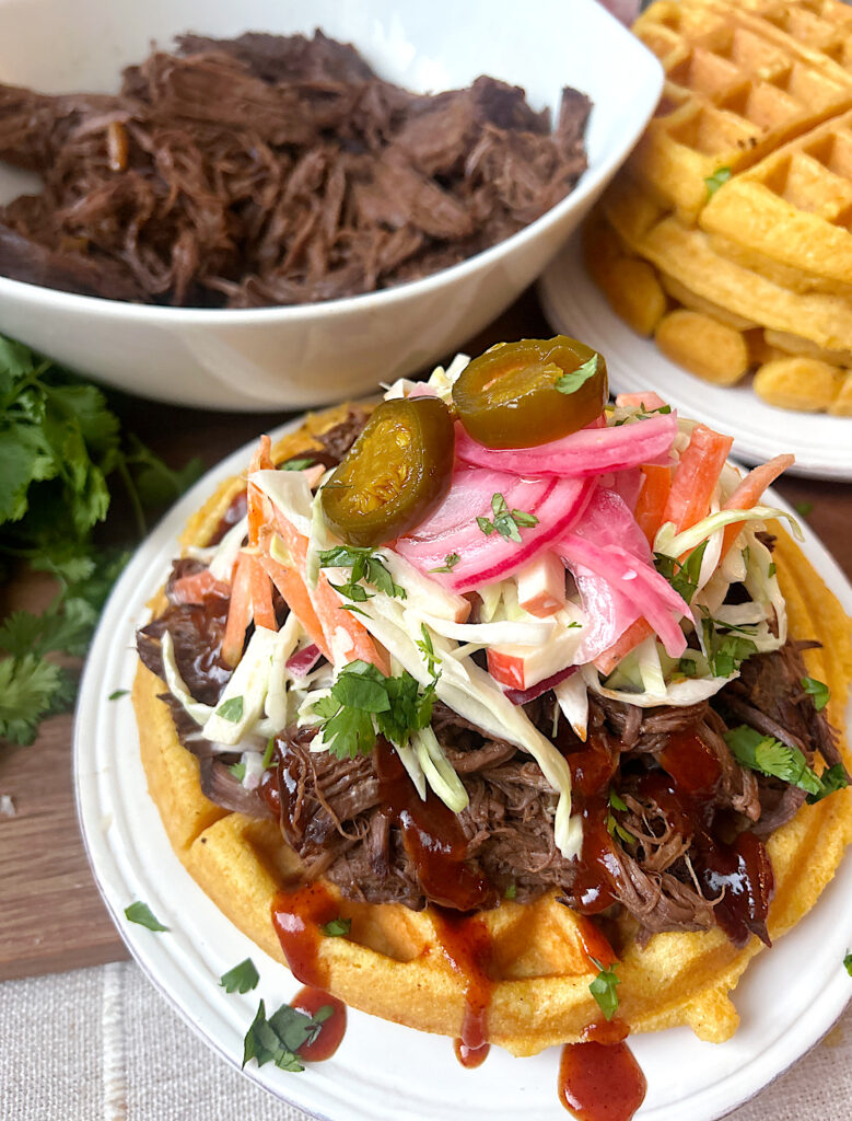 a cornbread waffle topped with shredded bbq meat, coleslaw and pickled onions