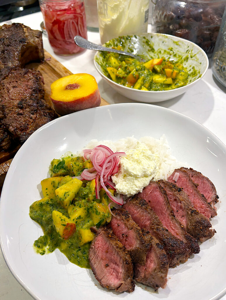 a rice bowl topped with whipped feta, peaches, chimichurri and sliced steak