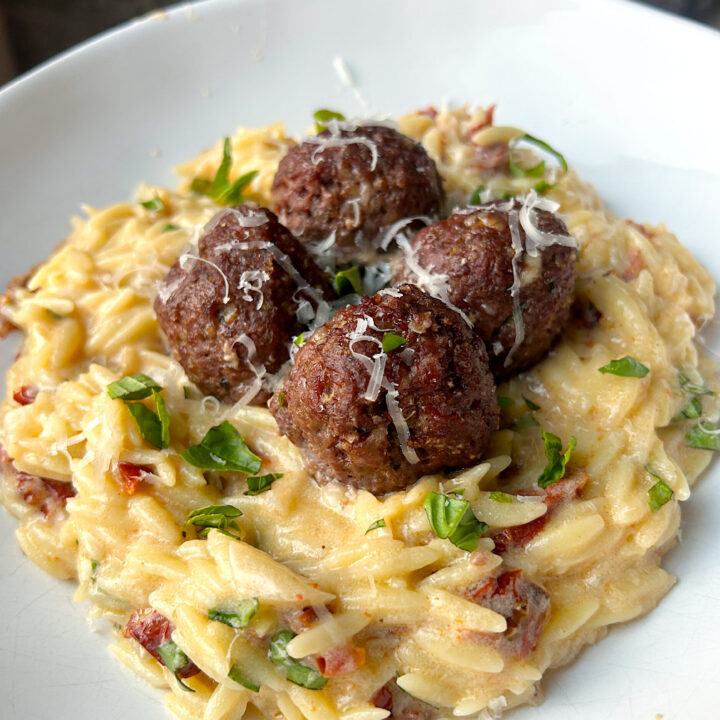 a white bowl of orzo pasta in a creamy white wine sauce with fresh basil and meatballs