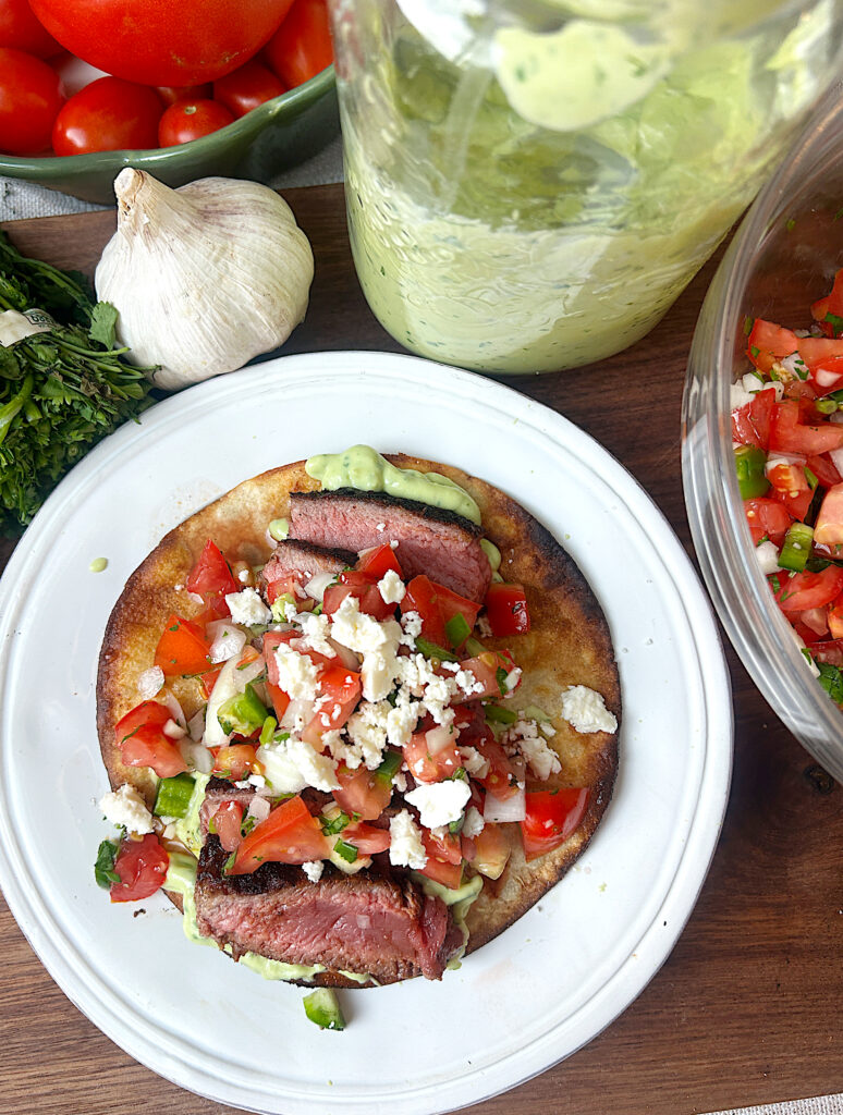 a white plate with a golden crisp steak tostada topped with pico de Gallo