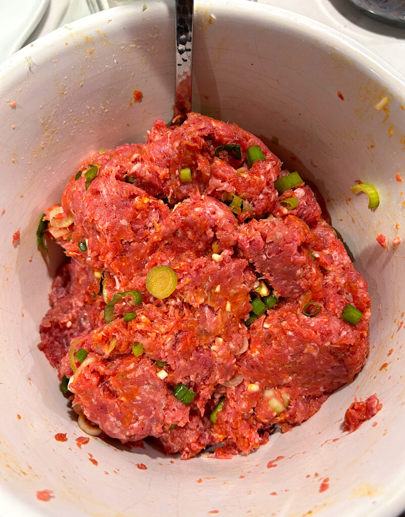 a bowl of ground meat mixed with spices and green onion