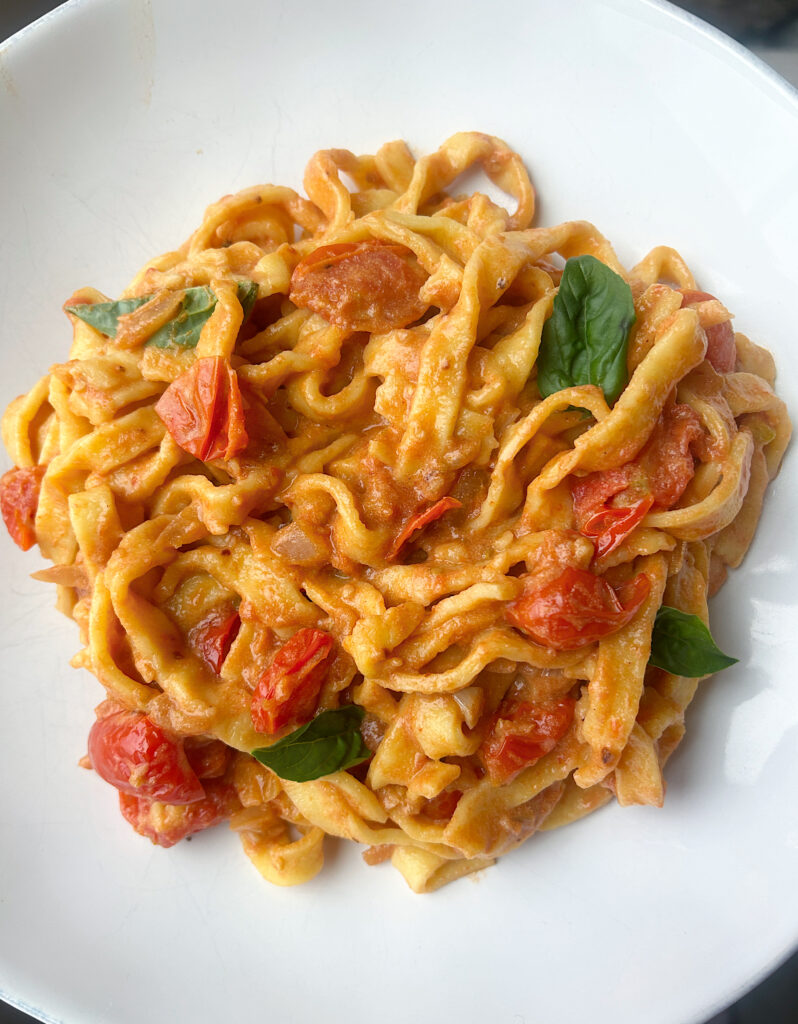 a white bowl of pasta with cherry tomato sauce and fresh basil