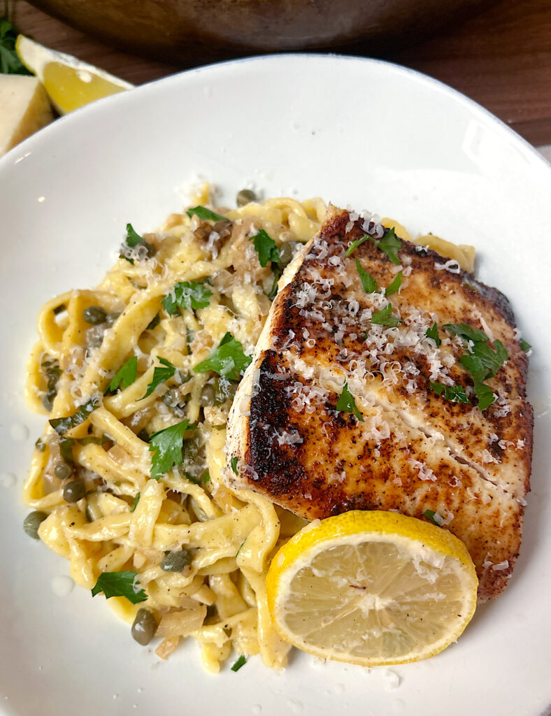 a white bowl of linguini noodles with lemon, capers and white fish