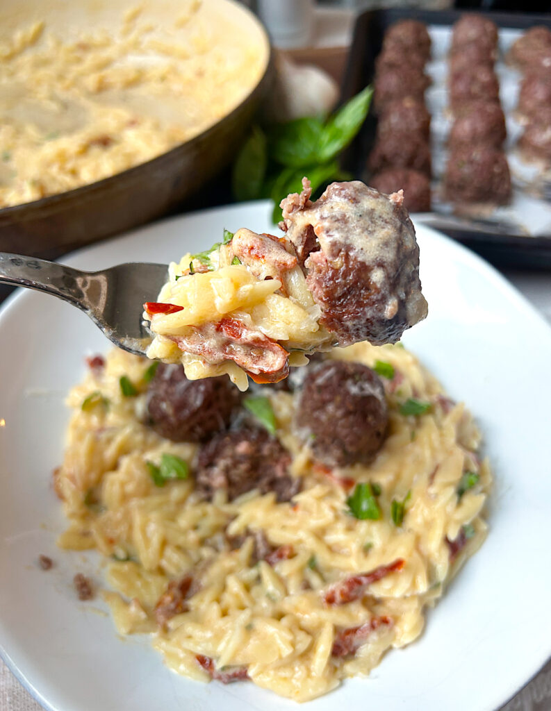 a white bowl full of creamy white wine orzo pasta with meatballs