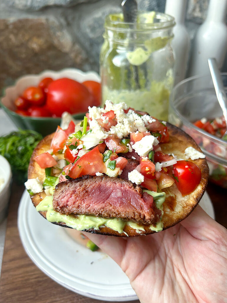 a crispy tostada with avocado sauce, pice de Gallo and sliced steak
