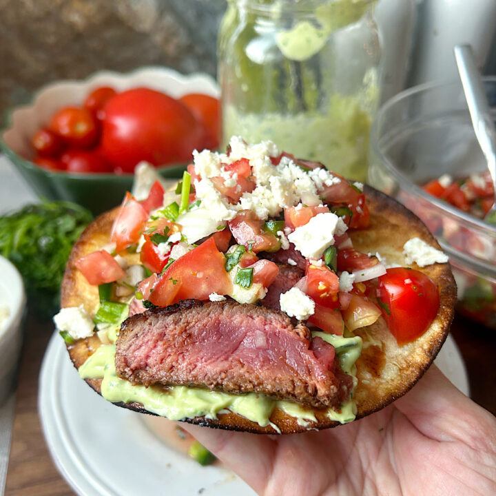 a crispy tostada with avocado sauce, pice de Gallo and sliced steak