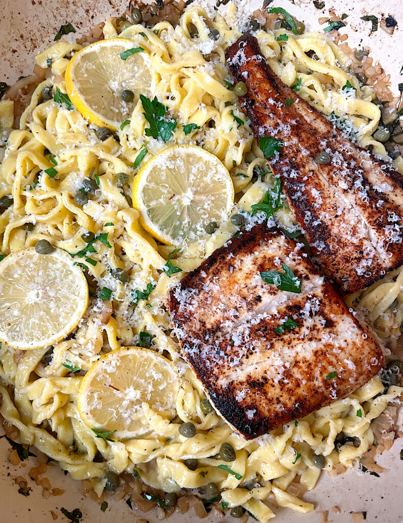 a skillet of lemon caper pasta with crispy halibut on top