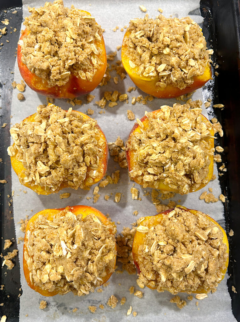 peach halves, filled with crumble topping on a baking sheet