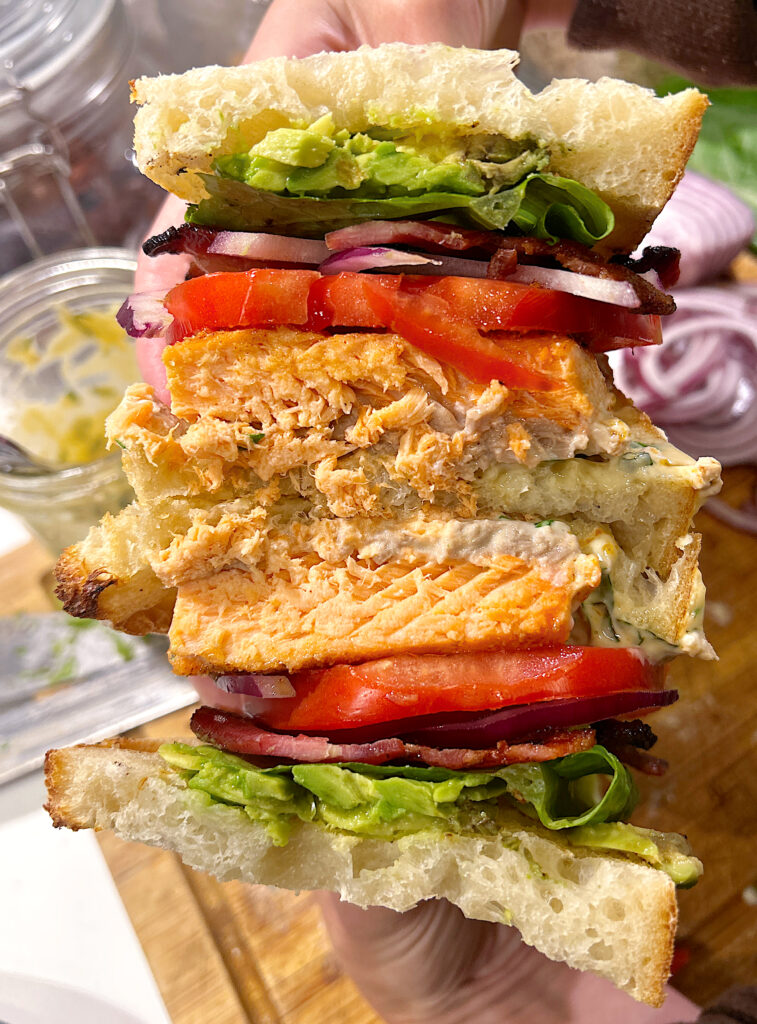 a sandwich cut in half with salmon, tomato, lettuce and bacon