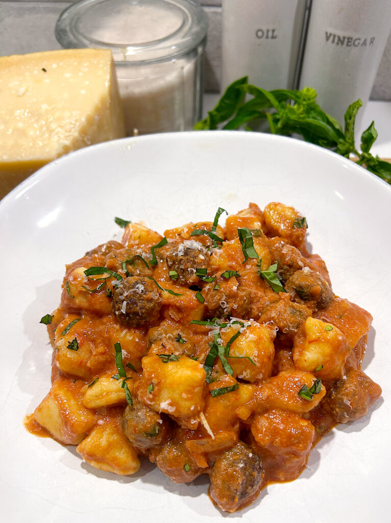 a white bowl with creamy tomato and basil gnocchi and venison meatballs