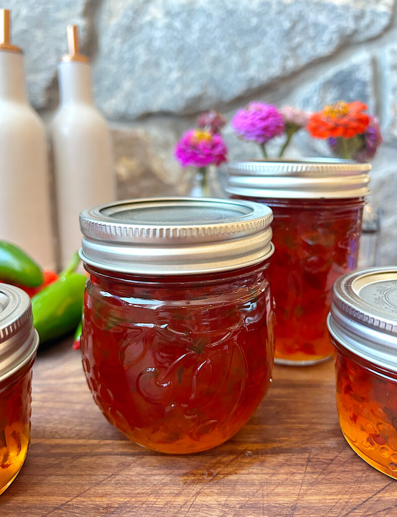 a couple jars of red pepper jelly on a wood board